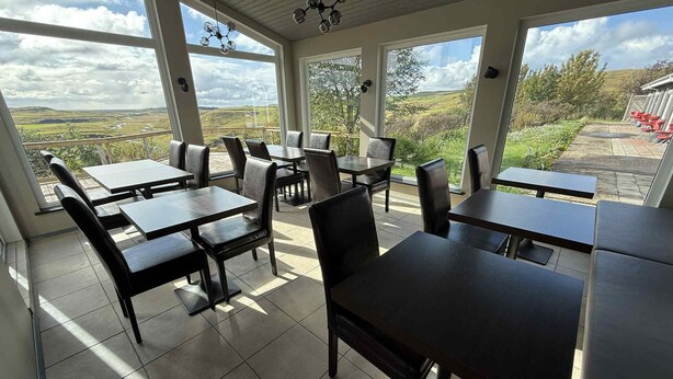 A restaurant with outdoor seating, large windows, and a view of the countryside. - Freya Farm (Storinupur)
