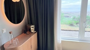 A room with a wooden console table, a coffee machine, and a view of a green landscape through a window with curtains. - Freya Farm (Storinupur)