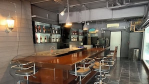 A bar area with a long counter, multiple stools, and a variety of bottles on shelves. - Highway Hotel (Hua Hin)