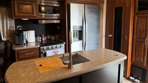 Een kleine keuken met een ingebouwde magnetron, fornuis, koelkast en spoelbak.