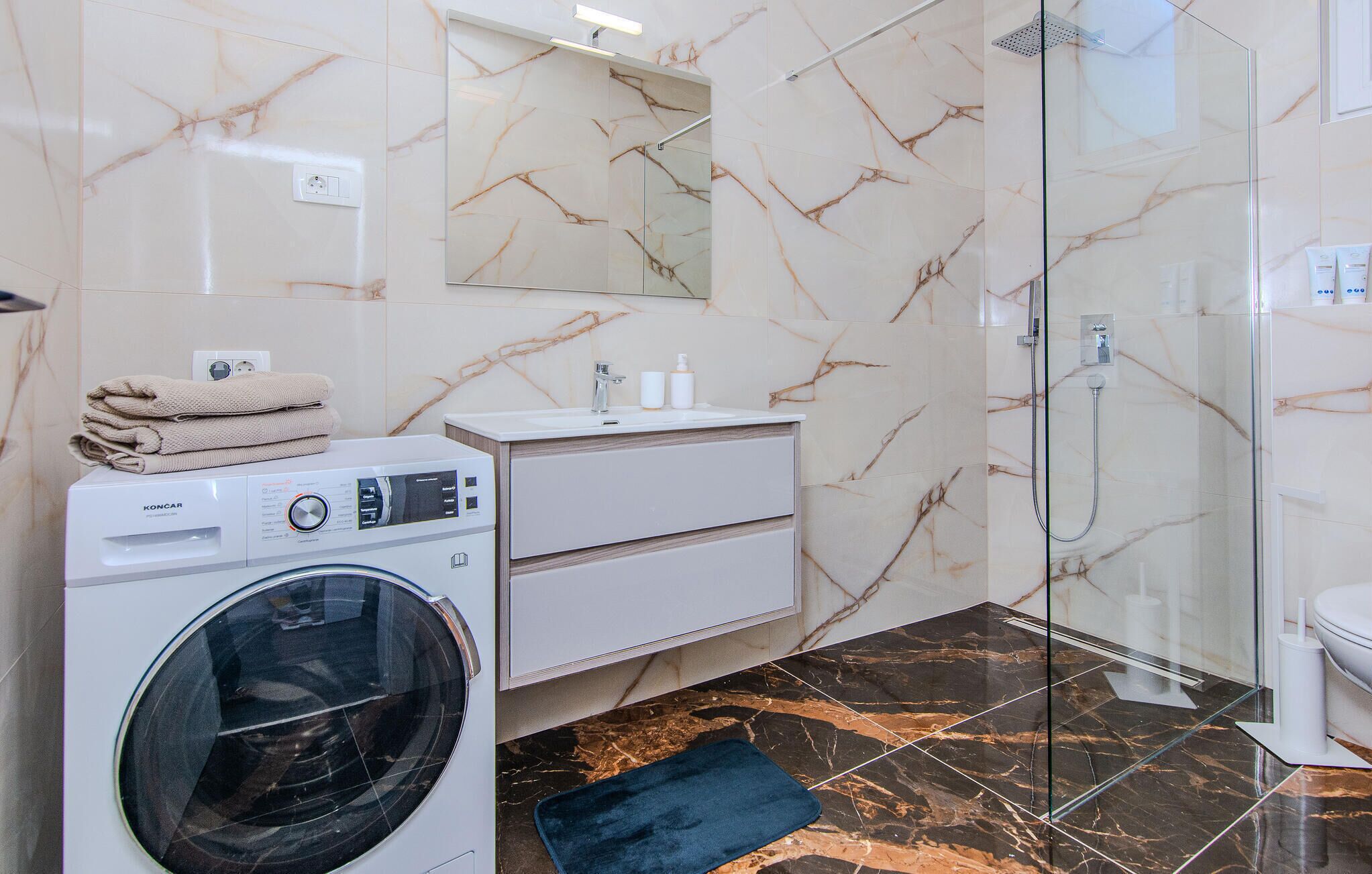 A modern bathroom with a washing machine, a sink, a mirror, and a shower.