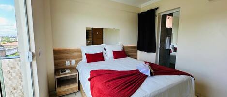 A hotel room with a bed, a nightstand, a mirror, and a door leading to a bathroom.