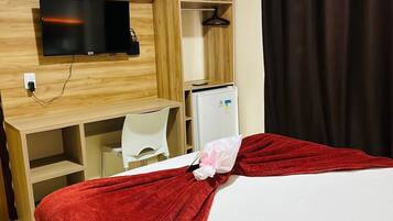 Ein Hotelzimmer mit Bett, einem an der Wand befestigten Fernseher, einem Schreibtisch mit Stuhl und einem Kleiderschrank.