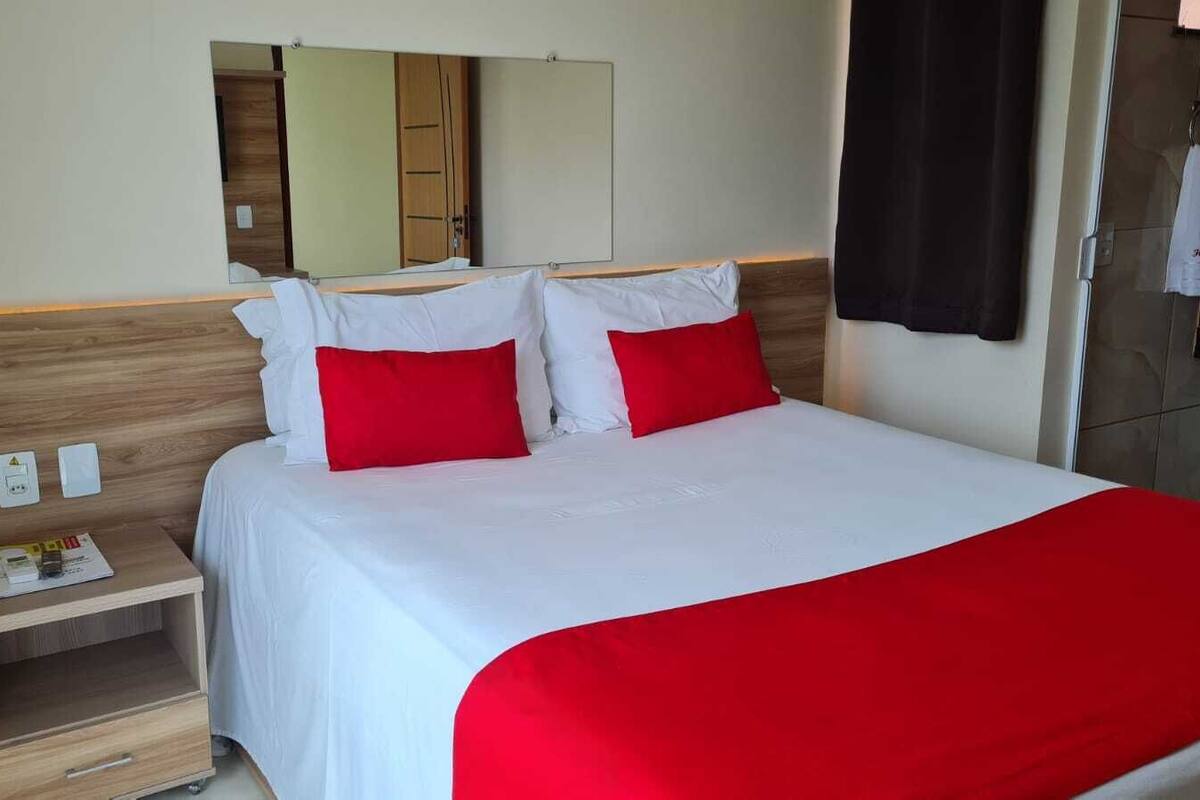 A hotel room with a bed, a nightstand, a mirror, and a bathroom door.