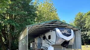 A covered RV with a "Open Range" logo, a covered outdoor area with a staircase, and two white chairs. - Cozy 2-bedroom mobile home in front of lake pleasant. (Beaver)