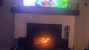 Una sala de estar con chimenea, televisor montado encima y una alfombra estampada en el suelo.