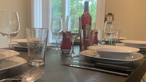 Mesa de comedor preparada para cuatro personas, con copas de vino, vasos de agua y una botella de vino.