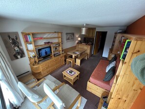 Ein gemütliches Wohnzimmer mit Fernseher, Holzmöbeln, einer Couch und einem Essbereich.