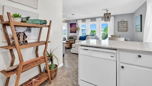 Eine moderne Küche mit weißer Arbeitsplatte, Holzregalen mit Pflanzen und Blick zum Wohnbereich.