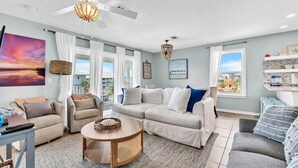 Ein geräumiges Wohnzimmer mit Deckenventilator, rundem Couchtisch und großem Fenster mit Blick auf die Stadt.