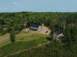 Une maison dotée d’une terrasse, entourée d’une forêt dense, et accessible par un sentier de terre.