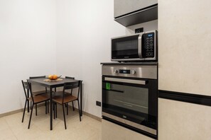 Een kleine keuken met een magnetron, oven en eettafel met stoelen.