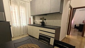 A modern kitchen with a black countertop, grey cabinets, and a black dining table with a woven placemat. - The little house in the hills - Appio/Tuscolano (Roma)