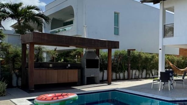 Un área de piscina moderna con una piscina rectangular, una pérgola de madera y una parrilla para barbacoa.