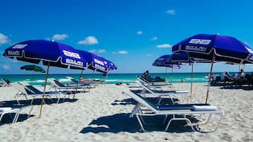 Une plage bordée de rangées de chaises longues et de parasols bleus portant l’inscription « BOULAN ».