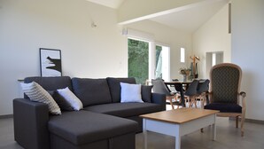 A modern living room with a grey sectional sofa, a wooden coffee table, and a patterned armchair. - Le Relais du Berger: House in the heart of the salt meadows (Céaux)