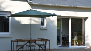 A patio with a table and chairs under a green umbrella, a sliding glass door, and a gravel ground. - Le Relais du Berger: House in the heart of the salt meadows (Céaux)