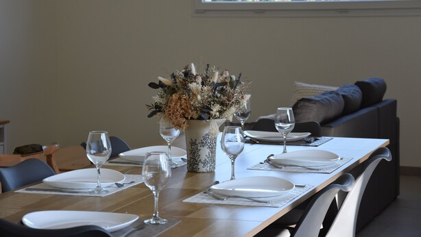 A dining table set with plates, cutlery, and wine glasses, with a vase of dried flowers in the center. - Le Relais du Berger: House in the heart of the salt meadows (Céaux)