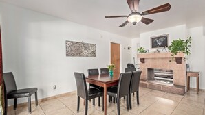 Un espace repas comprenant une table et des chaises en bois, un ventilateur de plafond, une cheminée et une œuvre d’art accrochée au mur.