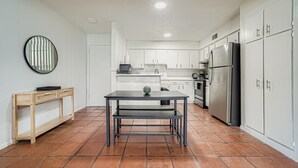 A kitchen with white cabinets, a black refrigerator, and a wooden table with a bench. - 2B Getaway | Sleeps 6 | Pool, Pkg | Walk Dtwn (Austin)