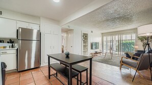 A modern kitchen with white cabinets, a stainless steel refrigerator, and a dining area with a dark table and bench. - 2B Getaway | Sleeps 6 | Pool, Pkg | Walk Dtwn (Austin)