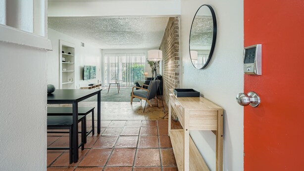 A modern living room with a dining area, a red door, and a brick wall. - 2B Getaway | Sleeps 6 | Pool, Pkg | Walk Dtwn (Austin)