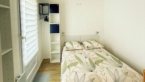 A bedroom with a bed, a wardrobe, a desk, and a hanging light fixture.