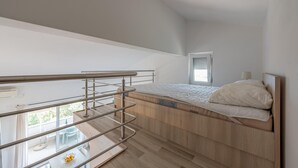 A compact bedroom with a bunk bed, a small window, and a balcony with a table and chairs.
