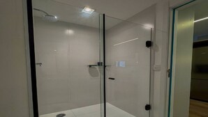 Een moderne badkamer met glazen deuren, een douchekop en een betegelde vloer.