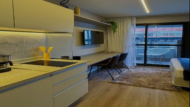 Een moderne keuken met een inbouwfornuis, een zithoek met een tafel en stoelen, en een groot raam met uitzicht op de stad.