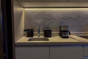 Eine Küche mit einer Granit Arbeitsplatte, einem Edelstahl-Spülbecken, einer Kaffeemaschine und einem Mülleimer.
