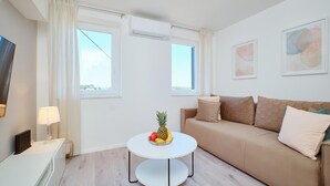 A modern living room with a sofa, two windows, a round table with fruit, and a lamp. - Awesome apartment in Mali Losinj with WiFi (Mali Losinj)