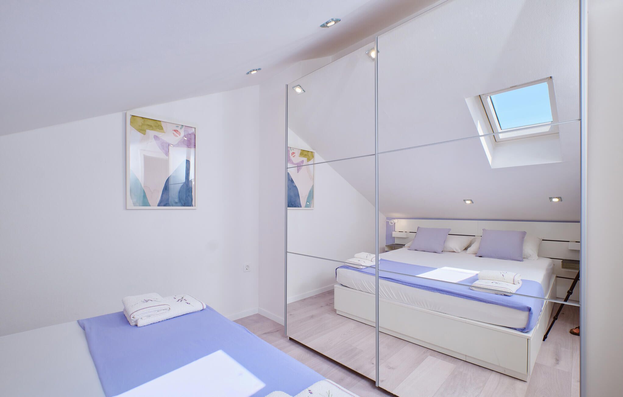 Une chambre moderne avec un grand miroir, un lit doté d’un matelas bleu et une petite fenêtre.