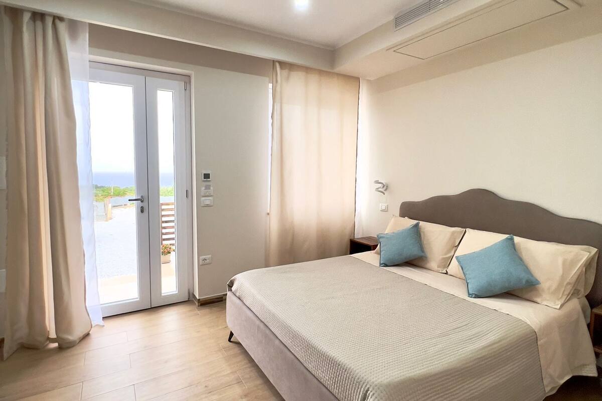 A bedroom with a large bed, a sliding glass door to the outside, and a ceiling fan.