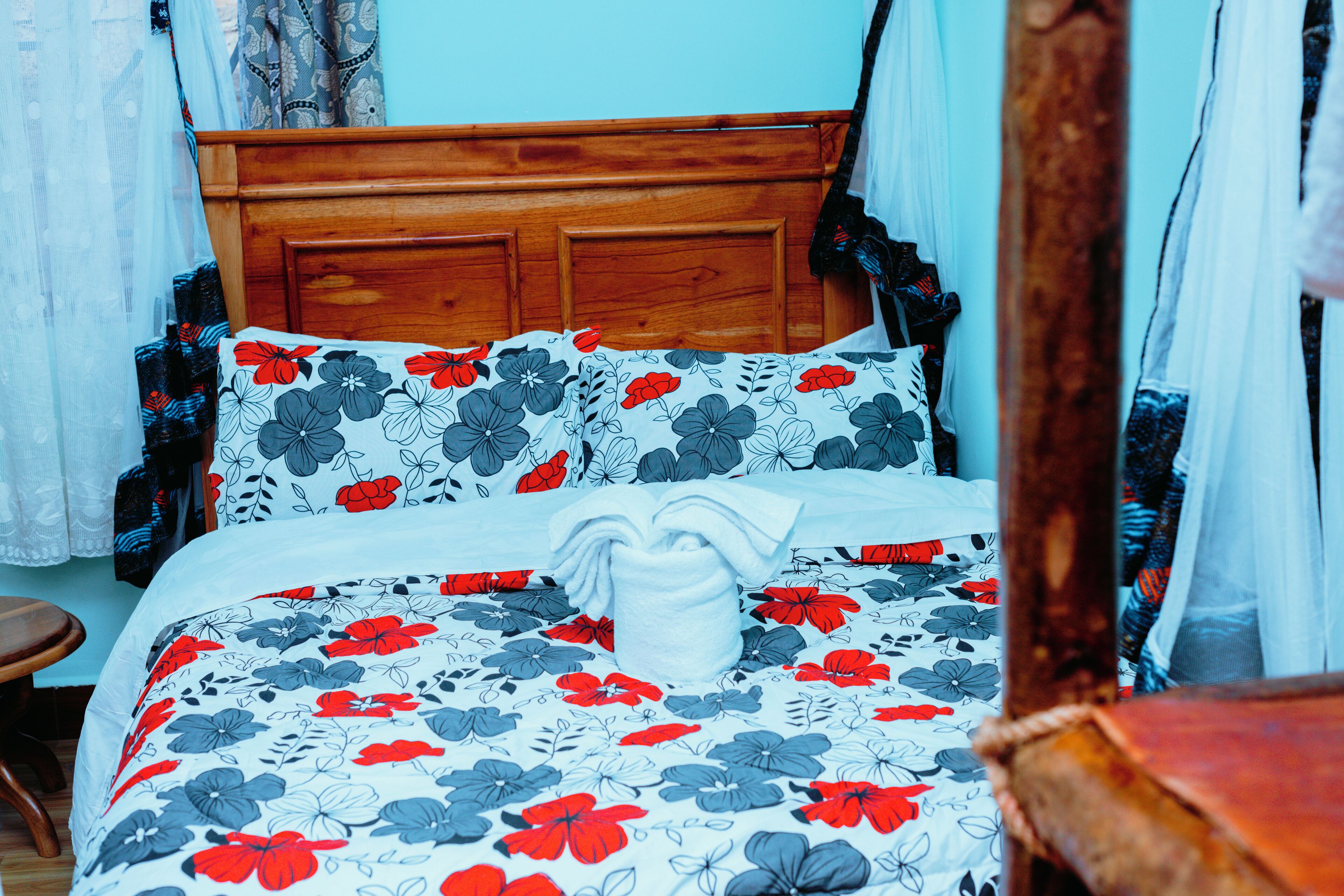 Una cama con cubrecama floral, cabecera de madera y almohada decorativa blanca.