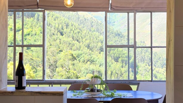 A dining area with a table and chairs, a bottle of wine, and a window with a view of a forested landscape. - Cottage | Pool | Mountain View | Jacuzzi (Arganil)