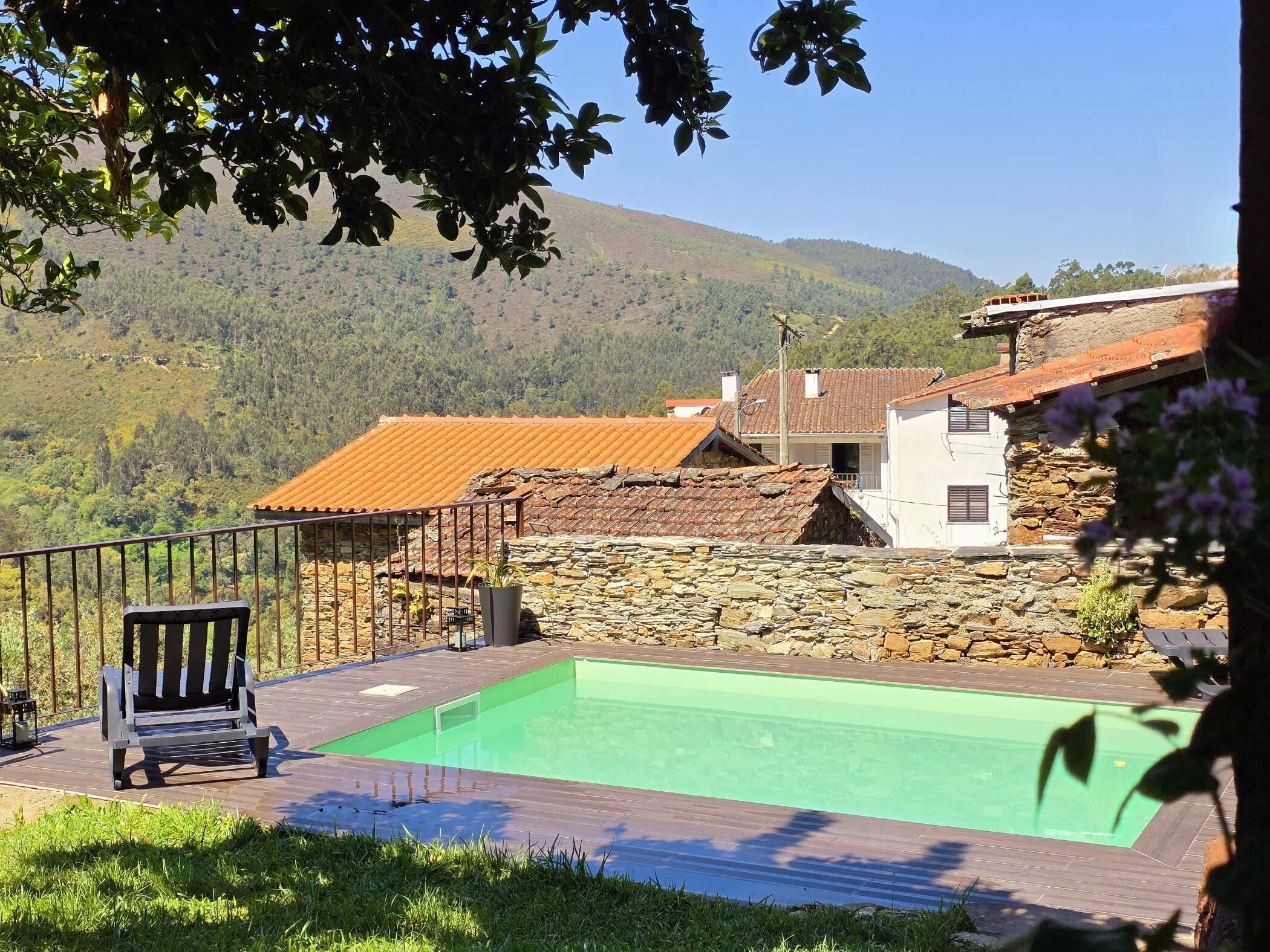Una piscina con una parete in pietra e un pontile in legno, immersa in un paesaggio montuoso.