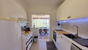 A compact kitchen with white cabinets, a built-in oven, a sink, and a window providing natural light. - Cottage | Pool | Mountain View | Jacuzzi (Arganil)