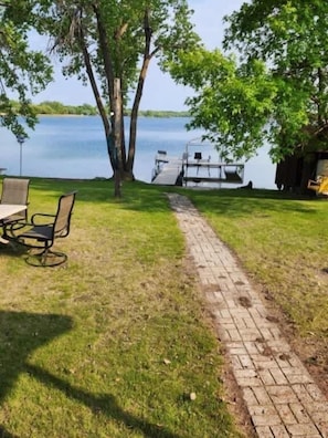 Un espace extérieur aménagé au bord du lac, avec un chemin pavé, une jetée et une table entourée de chaises.