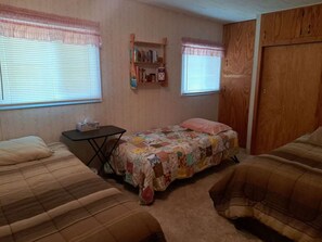 A bedroom with two beds, a small table, a bookshelf, and a wardrobe.