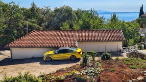 Ein gelber Wagen parkt vor einem Haus mit roten Ziegeldach, umgeben von Grün und mit freiem Blick auf das Meer.