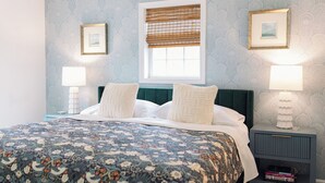 Una cama bien hecha con colcha estampada, dos lámparas de noche y una ventana con persianas.