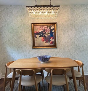 En matplats med ett träbord, sex stolar, en blå skål med mönster, en kristallkrona och en blomstermålning på väggen.