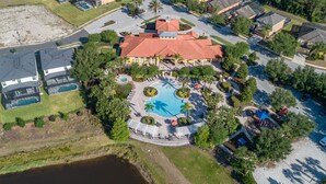 An aerial view of a resort with a central pool, surrounded by palm trees and a covered seating area.