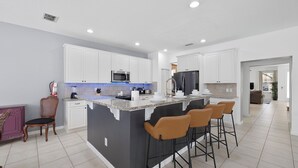 A modern kitchen with white cabinets, a central island with bar stools, a microwave, and a refrigerator.