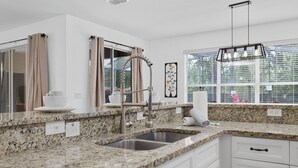 A modern kitchen with granite countertops, stainless steel appliances, and a large window with a view of greenery.