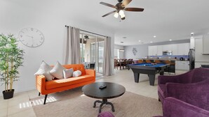 A modern living room with a pool table, orange sofa, and purple chairs.