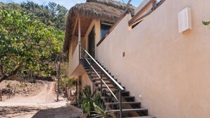 A staircase leading to a building with a thatched roof, surrounded by greenery and a dirt path.