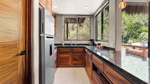 A modern kitchen with wooden cabinets, a black countertop, and a large window offering a view of greenery.