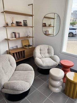 Un interior moderno con dos sillones grises, una estantería de madera, un espejo redondo y una pequeña mesa circular.